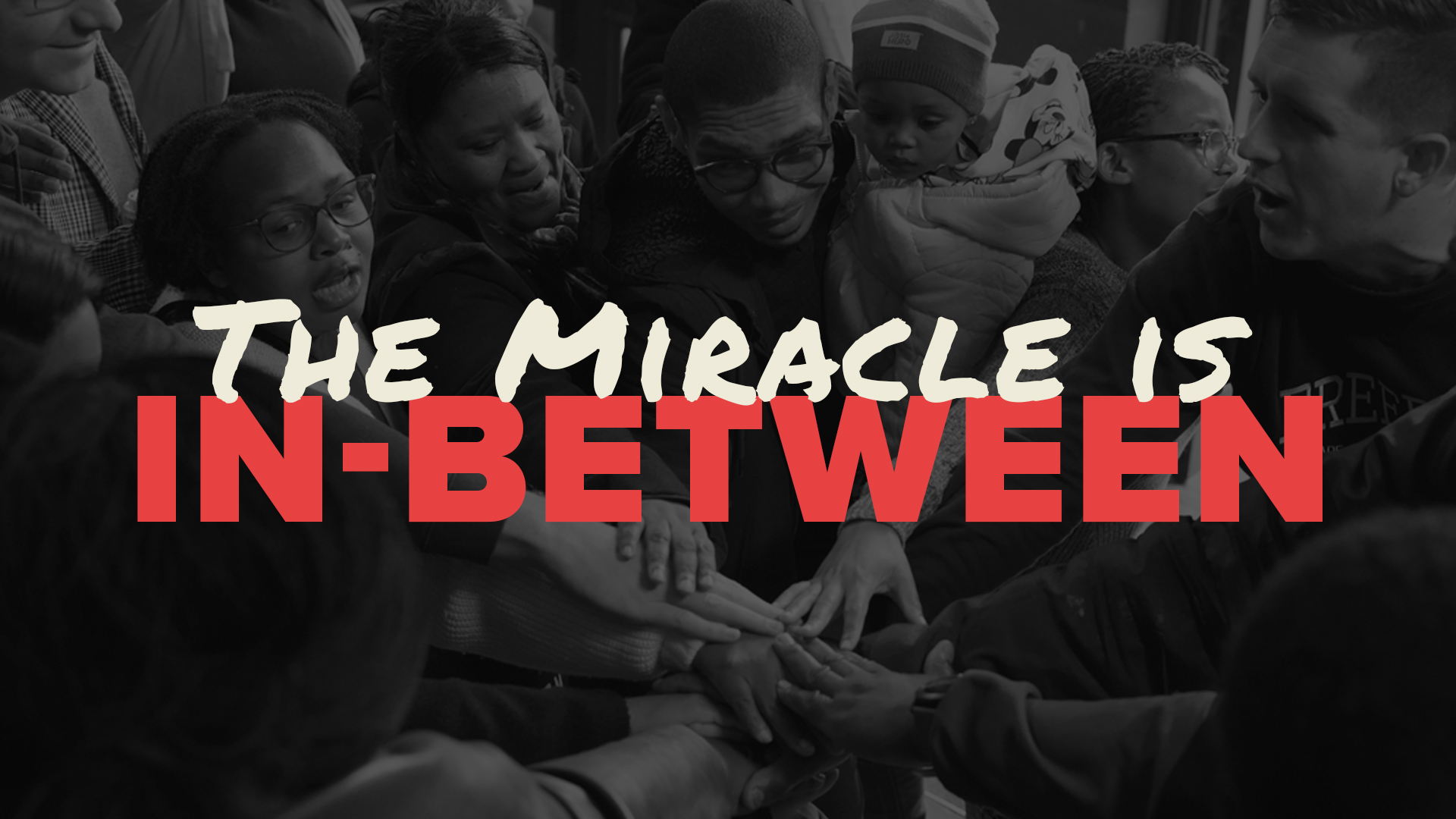 A picture of a group of people huddling together with the text "The Mieacle is In-Between" overlaid on it.