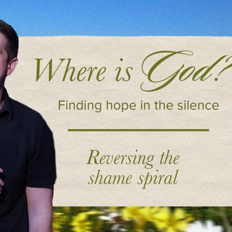 A smiling man in a dark blue polo shirt holds a microphone, standing in front of a blurred field of wildflowers under a blue sky. To his right, a beige notecard with a paperclip at the top reads, "Where is God? Finding hope in the silence" and below a line, "Reversing the shame spiral."