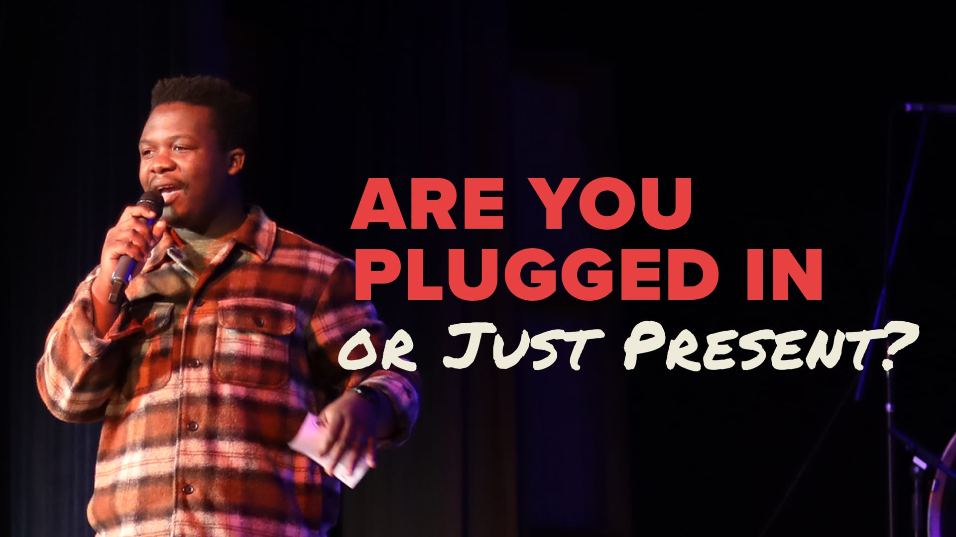 A photograph of a young man, Bradley Mubenga, wearing a plaid shirt and speaking passionately into a microphone on a dark stage. Large red and white text overlaid on the image reads: "ARE YOU PLUGGED IN OR JUST PRESENT?"