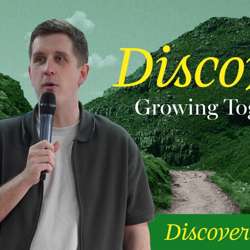 A man with short dark hair in a dark grey collared jacket over a white t-shirt holds a microphone and speaks, looking slightly to his left. He is positioned on the left side of the frame, with a stylized background of green, rolling hills and a dirt path winding through them. The sky is a muted green. Yellow text "Discover" in a script font is prominently displayed in the upper right, with "Growing Together" in a simpler white font below it. At the bottom right, "Discover Church" is written in green script font.